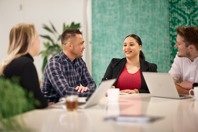Vier collega's die met elkaar in overleg zijn aan een lange tafel