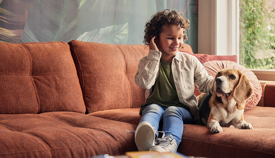 Een jong jongetje dat samen met zijn hond op de bank zit. Het jongetje aait de hond en kijkt blij