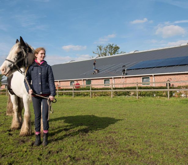 Mevrouw samen met haar paard in een weiland. Voor een verduurzaamd gebouw.