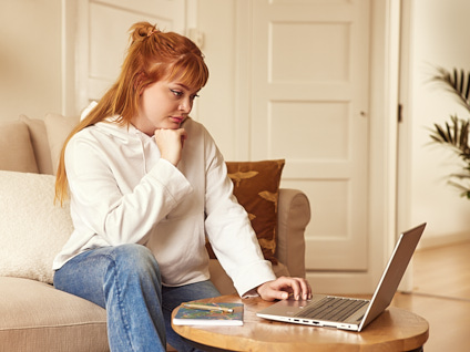 Vrouw zittend op de bank achter haar laptop die op de salontafel staat