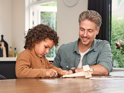 Man met kind aan tafel die bezig is met zijn speelvliegtuig