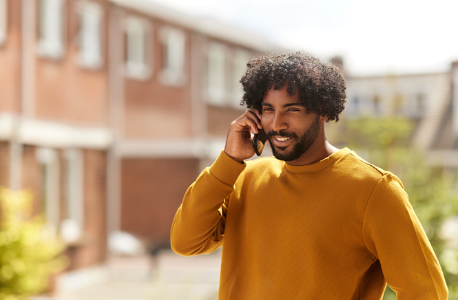 Jongeman die op het balkon van zijn VvE in de zon staat en aan het bellen is met een glimlach op zijn gezicht