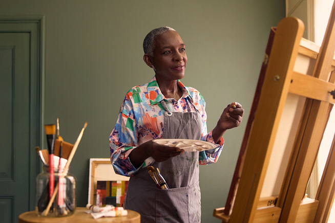 Vrouw met verfkwast en palet in handen kijkend naar een schildersdoek