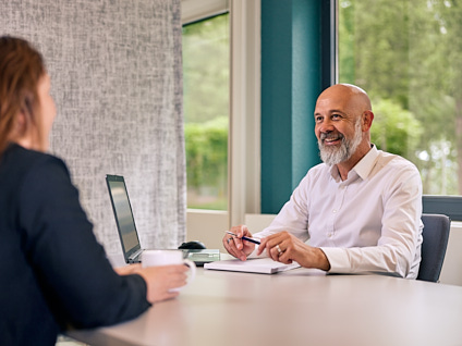 Mevrouw die in gesprek is met een financieel adviseur. De financieel adviseur zit achter zijn laptop met een glimlach