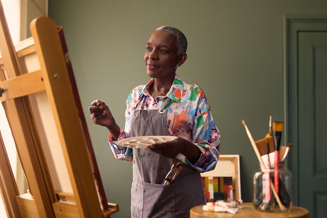 Vrouw met schilderspalet en kwast in haar handen kijkend naar haar schildersdoek