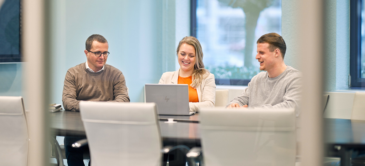 Drie collega's van SVn die glimlachend naar een laptop kijken tijdens een overleg