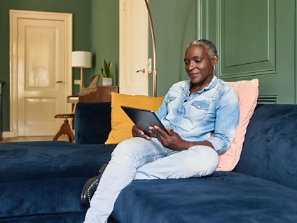 Vrouw lachend en zittend op de bank met tablet in haar handen