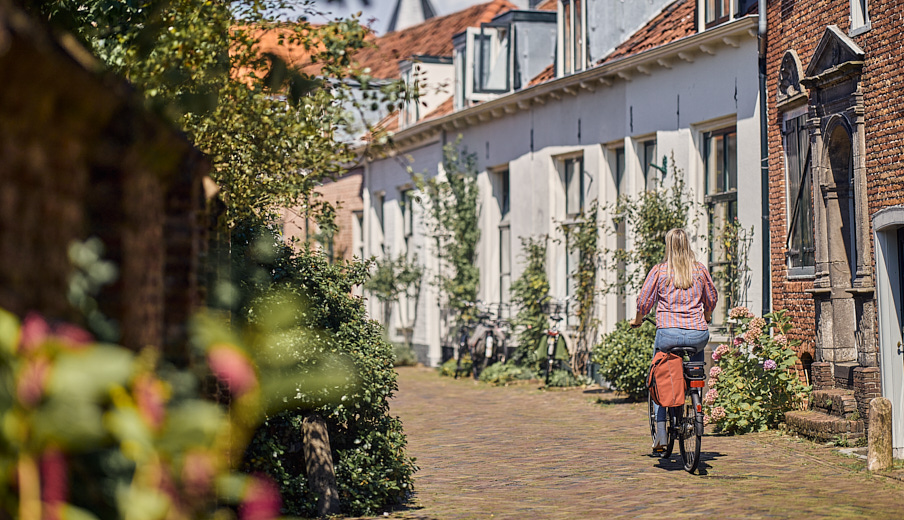 Een blonde dame die door een oude straat in de binnenstad fietst
