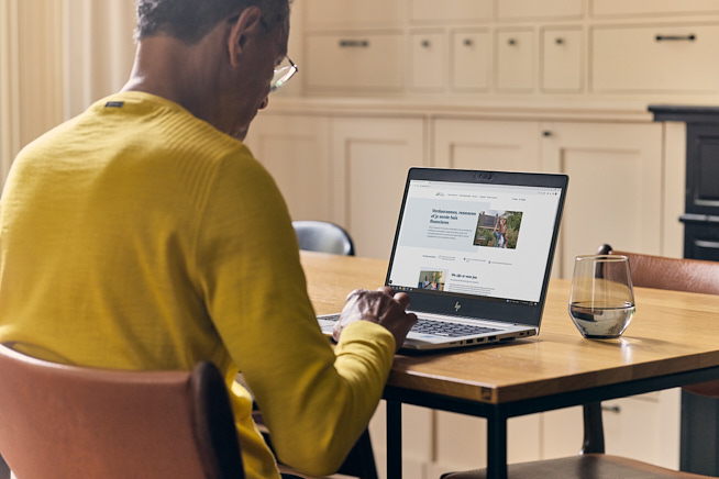 Man zittend aan tafel bezig achter zijn opengeklapte laptop