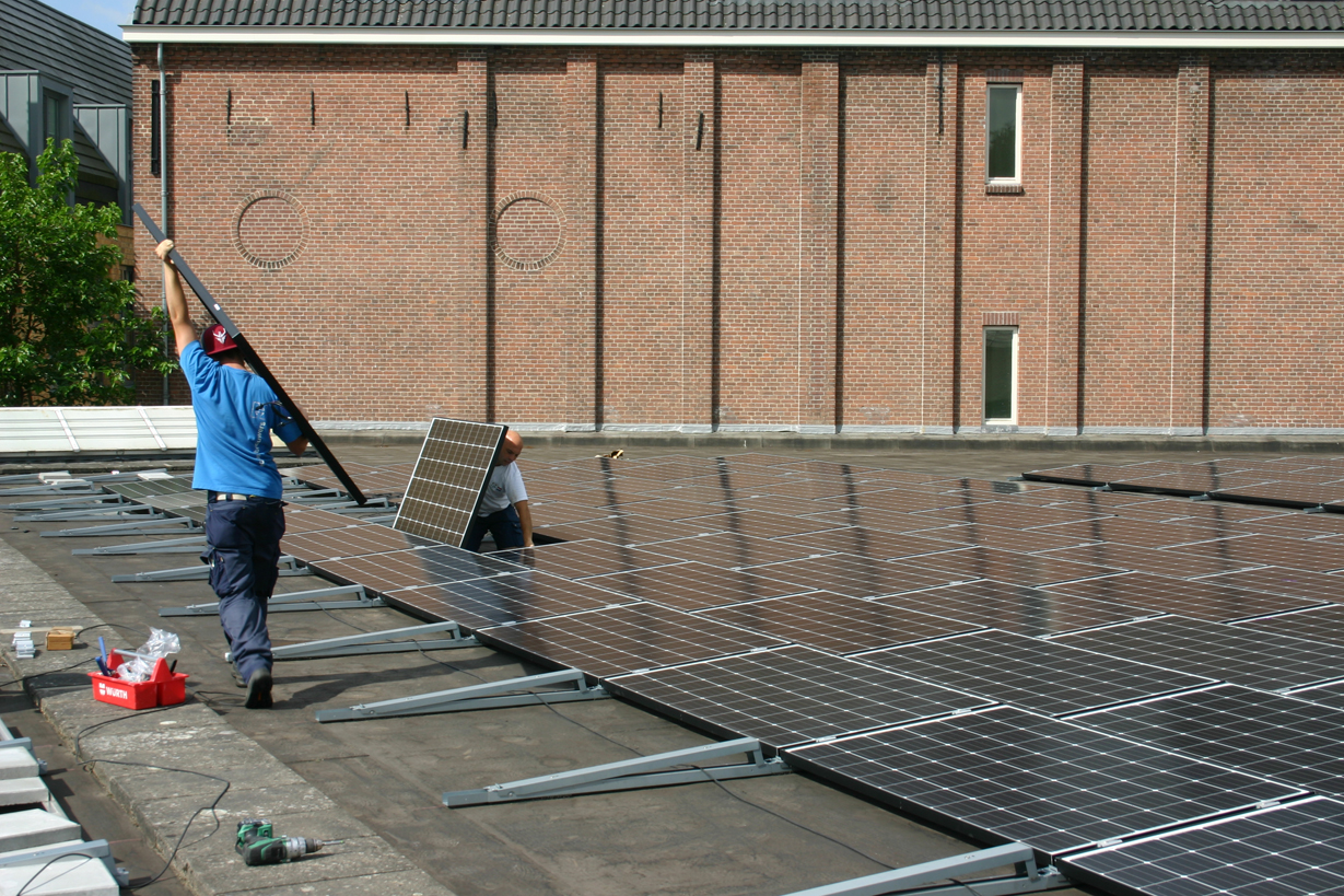 Man die een zonnepaneel tilt op een dak vol zonnepanelen voor Energie En Warmte Opwek
